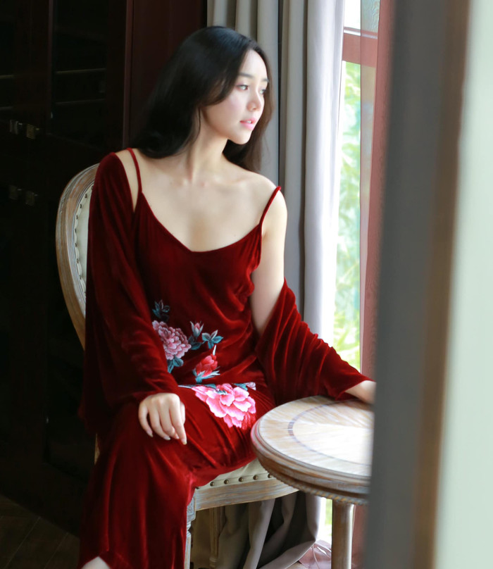 Tủ đồ của Quỳnh Kool còn có sự góp mặt của mẫu váy trễ nải chất liệu nhung, theo tông màu đỏ đô chủ đạo. Thiết kế này còn được tạo điểm nhấn bởi hoạ tiết hoa kích cỡ lớn cùng phần áo khoác ngoài đồng màu. Màu sắc cùng chất liệu của váy giúp Quỳnh Kool khoe khéo làn da mịn màng, trắng sáng và không chút khuyết điểm.