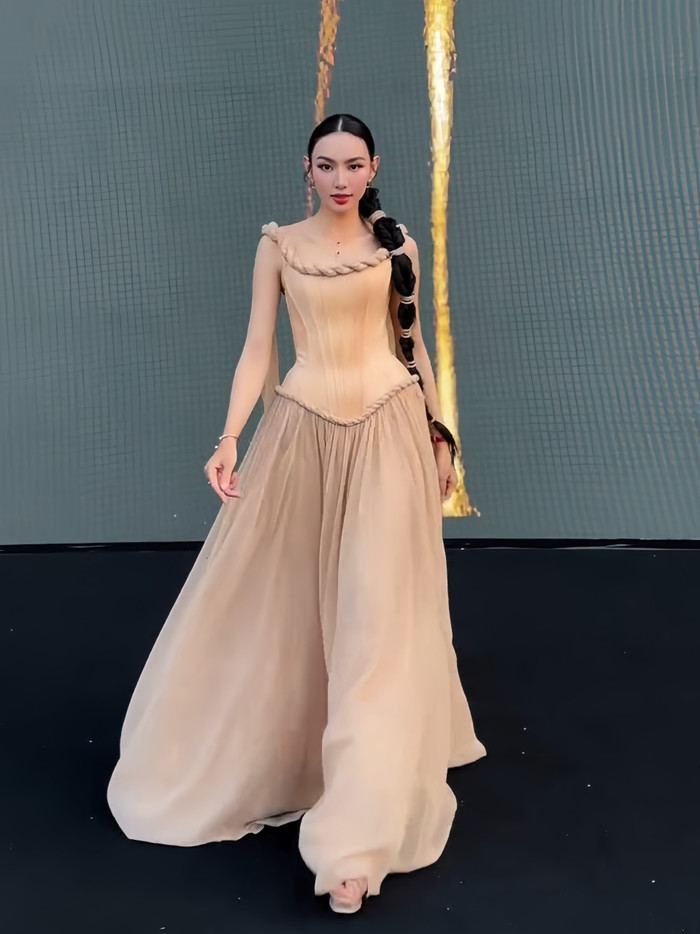 Đường viền cổ áo tạo điểm nhấn với dải dây thừng nối liền vải tulle bồng bềnh không chỉ tăng tính mạch lạc cho tổng thể tạo hình mà còn góp phần phô trọn khung xương quai xanh thon gọn của người mặc. Đồng điệu thiết kế của nhà mốt Lê Thanh Hòa, cô chọn kiểu tóc rẽ ngôi giữa, tết bím cực sành điệu với bản dây thừng mảnh.  