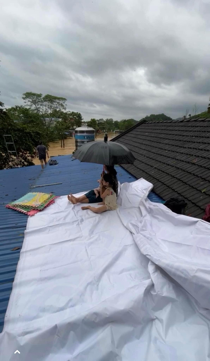 Hình ảnh ba mẹ con che chở nhau dưới cơn mưa nặng hạt, nước lũ không ngừng dâng lên khiến ai cũng xót thương. Ảnh: Võ Hồng Ly