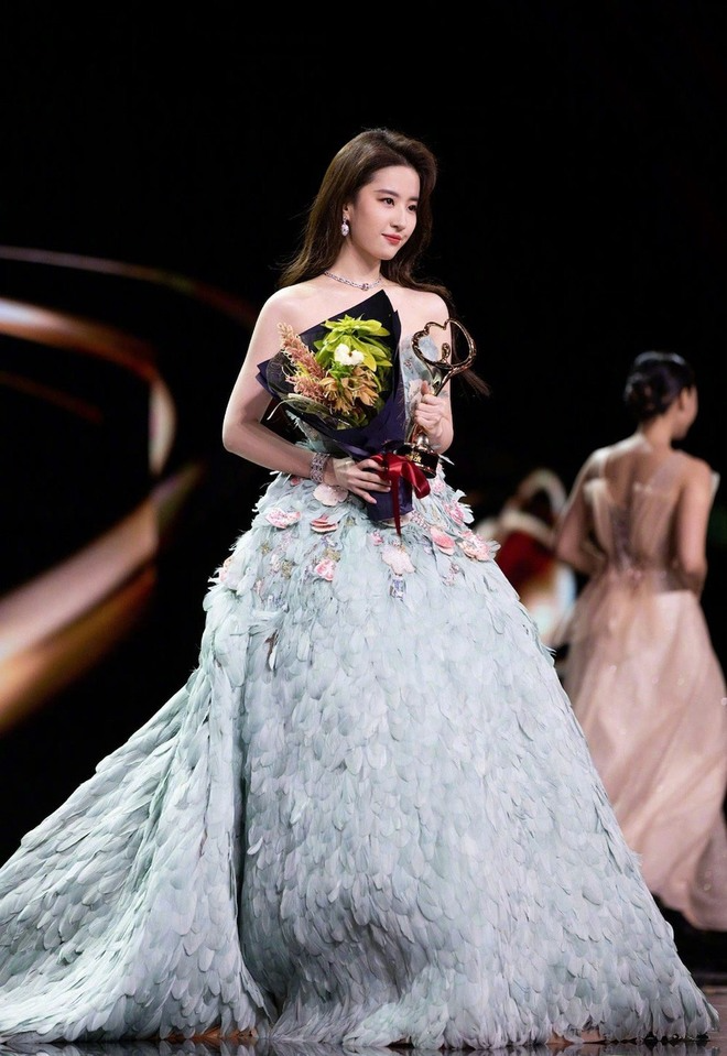 Lưu Diệc Phi phủ sóng mạng xã hội với chiếc váy xanh của thương hiệu Elie Saab ở Đêm hội Weibo. Mẫu váy được đính bằng hàng nghìn chiếc lông vũ cao cấp, phom dáng chữ A của thiết kế giúp 'thần tiên tỷ tỷ' trở nên thon gọn thấy rõ. Đồng thời, kiểu áo quây cúp ngực dễ dàng giúp mỹ nhân họ Lưu tự tin khoe vai trước ống kính. 