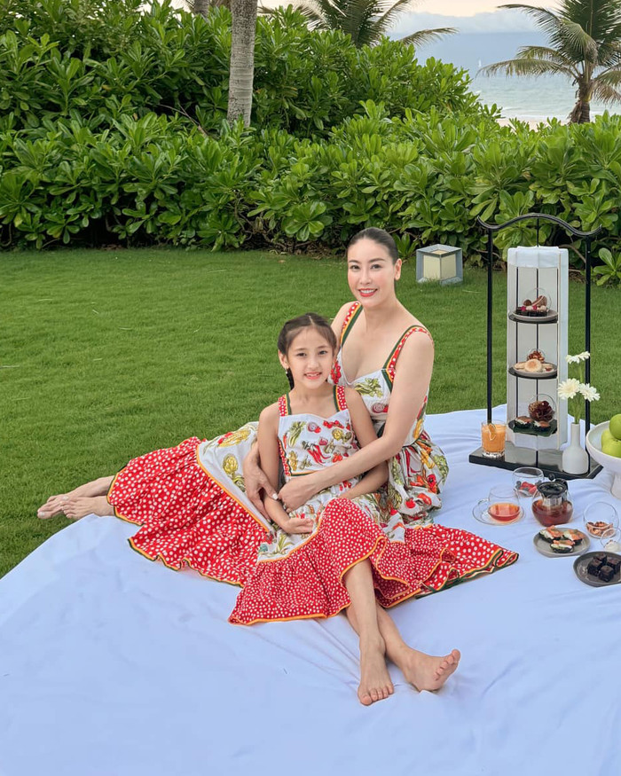 Hà Kiều Anh cùng con gái Huỳnh Viann diện mẫu đầm hai dây xoè theo tông màu chủ đạo trắng - đỏ. Thiết kế này được tạo điểm nhấn bằng hoạ tiết đầy màu sắc, toát lên phong thái hoàng gia. Nó là sản phẩm của một thương hiệu đình đám trên thế giới. Hà Kiều Anh đã phải chi khoảng 20 triệu đồng để sắm mẫu váy rực rỡ này cho con. Thiết kế váy của cựu Hoa hậu Việt Nam lại có phần đắt đỏ hơn, có mức giá khoảng 20 triệu đồng.