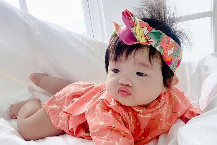 Winnie - con gái Đông Nhi cũng được mẹ hết mực cưng chiều. Trong một khung hình, nhóc tỳ gây chú ý khi đeo chiếc khăn lụa với hoạ tiết nổi bật được kết thành băng đô cài tóc. Thiết kế này đến từ 'nhà mốt' đình đám xuất thân từ Pháp và được bán với mức giá gần 7 triệu đồng. Hoạ tiết rực rỡ trên chiếc khăn lụa được Winnie diện ăn khớp hoàn toàn với màu sắc của trang phục, giúp con gái đầu lòng của Đông Nhi thêm phần nổi bật và rạng rỡ.