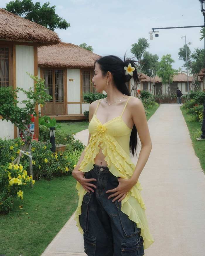 Trong bộ ảnh mới nhất được trình làng, Hoa hậu Thùy Tiên lăng xê mốt áo xẻ tà, vạt dài cách điệu. Xu hướng này được phái đẹp toàn cầu yêu thích thời gian gần đây bởi độ bắt mắt cũng như chất liệu và kiểu cách độc đáo. Phối cùng thiết kế hai dây bản mảnh nhuộm sắc vàng rực rỡ, nàng hậu diện quần denim jeans ống rộng điểm xuyết nhiều túi hộp phá cách. Theo tìm hiểu, trọn bộ áo quần được ra mắt giới mộ điệu với giá 4.3 triệu đồng.  