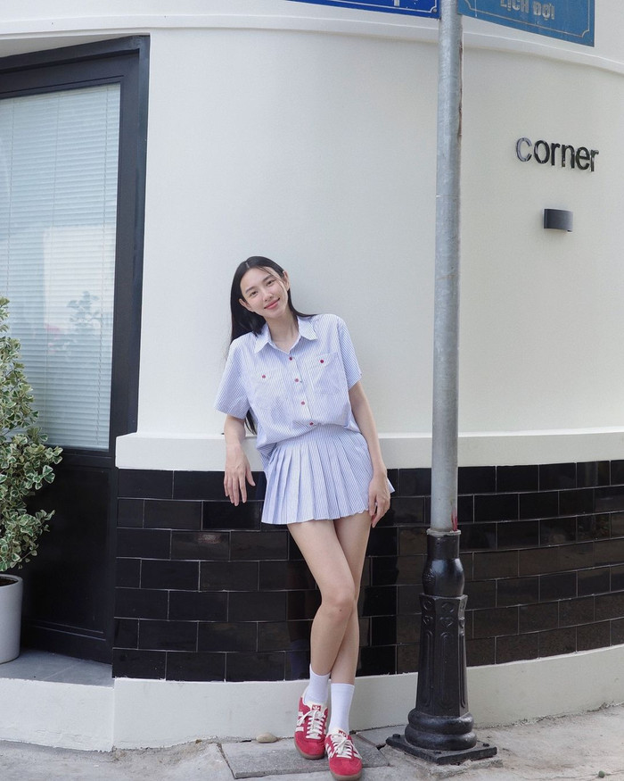 Đi theo tôn chỉ Basic but Chic, Hoa hậu Thùy Tiên thả dáng giữa phố trong bản phối sơ mi và chân váy xếp li kẻ sọc tông xanh. Cúc áo đỏ điểm tô trên nền vải thô Hàn kết hợp kiểu may đứng phom mang tính ứng dụng cao. Trọn bộ áo váy mà nàng hậu chọn đến từ thương hiệu nội địa Việt Nam. Khung giá công bố nằm trong phân khúc tầm trung khoảng 580 nghìn đồng.