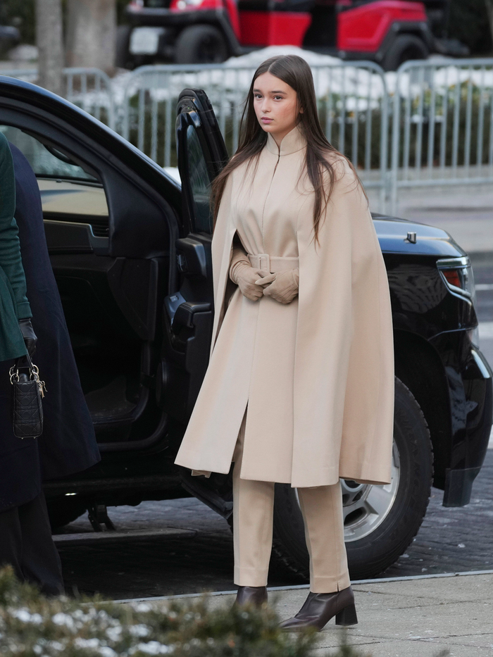 Cô bé diện áo choàng màu be dài đến đầu gối có thiết kế cổ đứng kết hợp với thắt eo bằng đai bản dày cùng tông tối giản. Trang phục được phối với quần đồng màu và bốt da đen gót thô, tạo nên vẻ ngoài hiện đại và tinh tế.