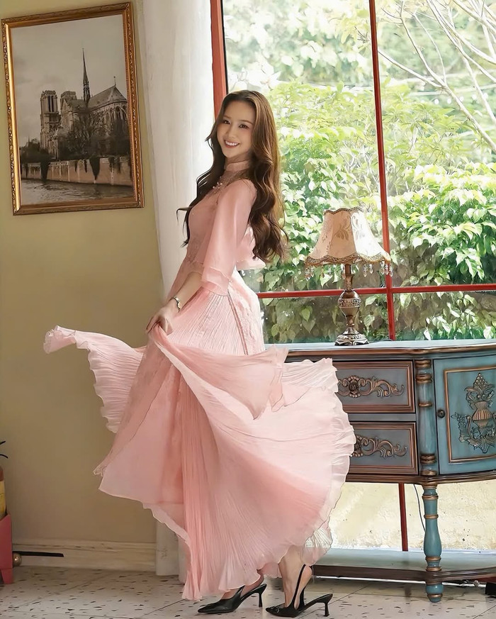 Hoa hậu Bảo Ngọc trở nên ngọt ngào, nữ tính như một nàng thơ khi khoác lên người chiếc áo dài cách tân màu hồng pastel. Phần tà của thiết kế này được đính kết thêm nhiều lớp vải mỏng tựa một chiếc chân váy, tạo cảm giác mềm mại và không kém phần bay bổng. (Ảnh: FBNV)
