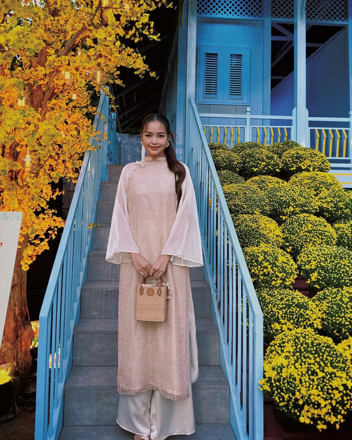 Hoa hậu Ngọc Châu diện áo dài mang tông màu beige đơn giản nhưng không kém phần thanh lịch. Phần tay áo của thiết kế này được làm theo form dáng loe, tạo cảm giác mềm mại, nữ tính. Hoa hậu Ngọc Châu còn phối cùng phụ kiện túi xách mang chất liệu cói đan lát tỉ mỉ. (Ảnh: FBNV)