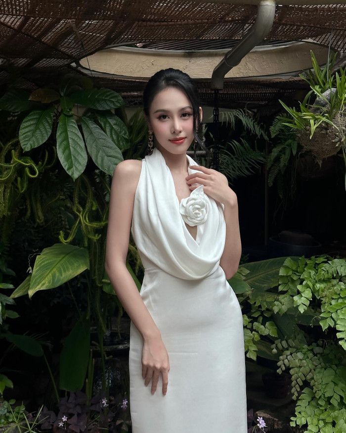 Trong bức ảnh, cô diện chiếc đầm trắng cổ yếm mềm mại với điểm nhấn hoa vải nổi bật ở phần ngực, tạo nên vẻ nữ tính và sang trọng. Chất liệu vải satin cao cấp mang lại cảm giác nhẹ nhàng, mềm mại và ánh sáng bắt mắt, giúp tôn lên vóc dáng thanh thoát của người mặc.