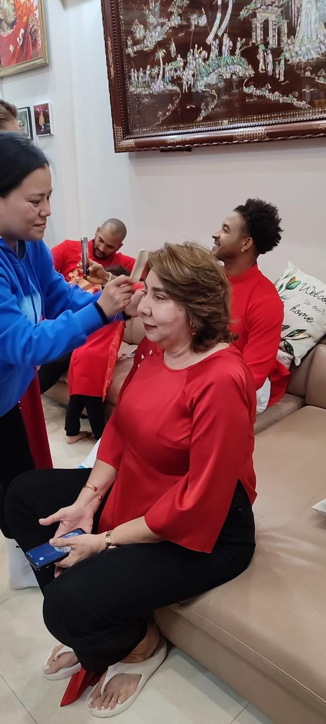 Mẹ vợ của Nguyễn Xuân Son diện áo đỏ có thiết kế giống với áo bà ba của phụ nữ Việt Nam. Điều này thể hiện sự chuẩn bị chu đáo của gia đình nam cầu thủ, khi mọi người cùng nhau trang điểm và chỉnh sửa trang phục để hoàn thiện vẻ ngoài trước thềm Tết. Đây không chỉ là khoảnh khắc thể hiện nét đẹp văn hóa mà còn là minh chứng cho sự hòa nhập của gia đình anh vào đời sống Việt Nam. Ảnh: Nam Định FC