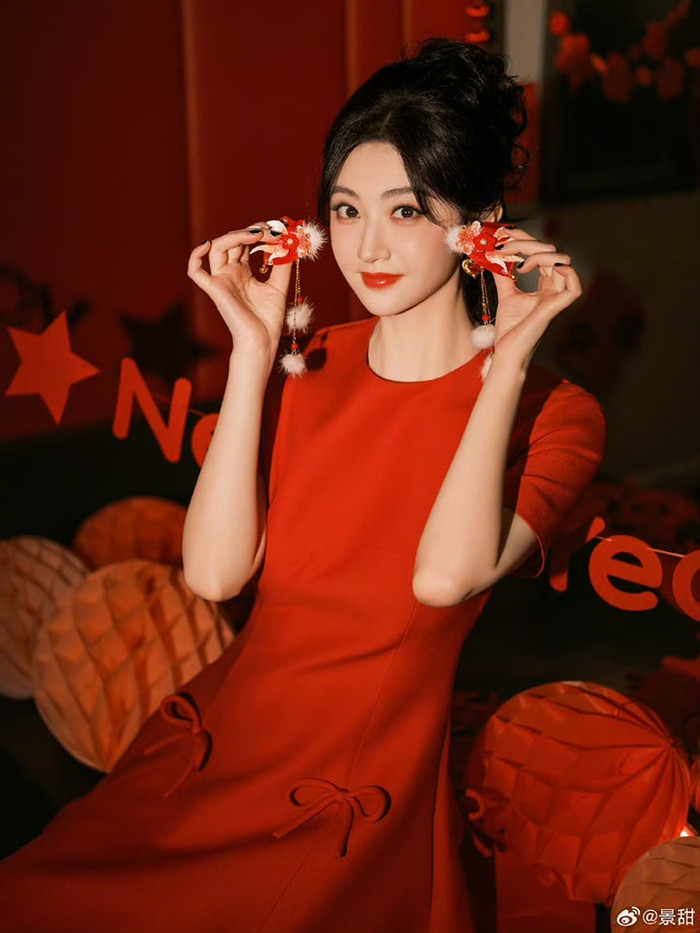 Cảnh Điềm cũng chọn sắc đỏ cho bộ ảnh mừng Xuân. So với Dương Mịch, trang phục Cảnh Điềm chọn có vẻ đơn giản hơn, với chiếc đầm dáng chữ A, điểm nhấn là 2 chiếc nơ bản to ở phần thân váy. Kiểu trang điểm sắc sảo với màu son đỏ nổi bật giúp gương mặt đại mỹ nhân Bắc Kinh thêm phần bừng sáng.