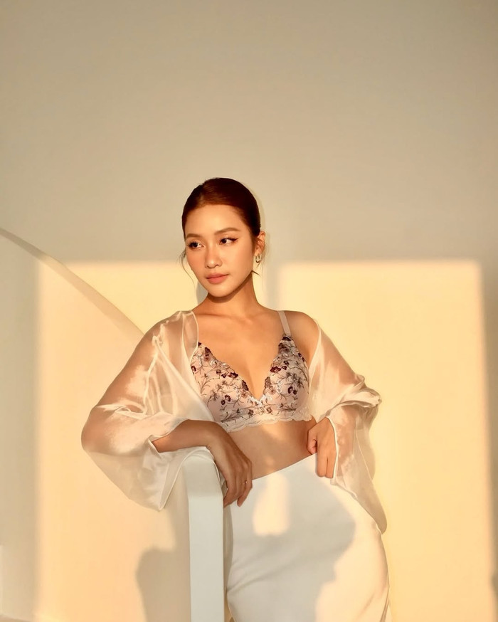 Ngoài áo bra trơn, màu đơn sắc, Khả Ngân không ngần ngại thử sức ở thiết kế mang hoạ tiết hoa nhí, điểm xuyến chi tiết ren trên phần vạt áo. Nữ diễn viên phối item này cùng chân váy dài mang tông màu trắng chủ đạo. Đặc biệt, tổng thể tạo hình của Khả Ngân thêm phần gợi cảm khi kết hợp thêm mẫu áo voan lụa chất liệu mỏng manh, xuyên thấu, để lộ lấp ló da thịt. (Ảnh: FBNV)