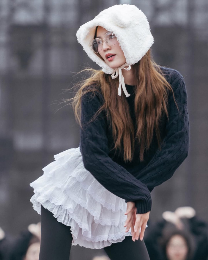 Chuyển sang không khí se lạnh ngoài trời, Ninh Dương Lan Ngọc thử nghiệm phong cách feminine vintage với mũ bonet lông trắng kiểu teddy bear, kết hợp áo len cable knit đen dài tay và váy trắng xòe tầng ren cầu kỳ. Item váy này, lấy cảm hứng từ xu hướng balletcore, có lớp layer ren chồng chéo tạo độ phồng tự nhiên, dễ dàng mix với tất da đen và boots chunky để cân bằng sự nữ tính. Ảnh: IGNV