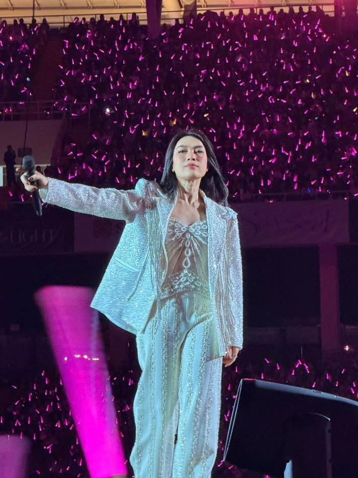 Mỹ Tâm mở màn bằng set đồ trắng toàn thân ấn tượng: blazer dài phủ sequin dày đặc, áo crop top chi tiết thắt nơ tinh tế và quần ống suông rộng cùng chất liệu sequin. Bộ trang phục này phản chiếu ánh sáng mạnh mẽ, phù hợp với phần mở đầu hoành tráng trên bàn nâng và catwalk dài. Thiết kế cấu trúc rõ ràng giúp Mỹ Tâm di chuyển thoải mái, đồng thời tạo cảm giác quyền lực và thanh lịch trên không gian sân vận động rộng lớn. Ảnh: FBNV