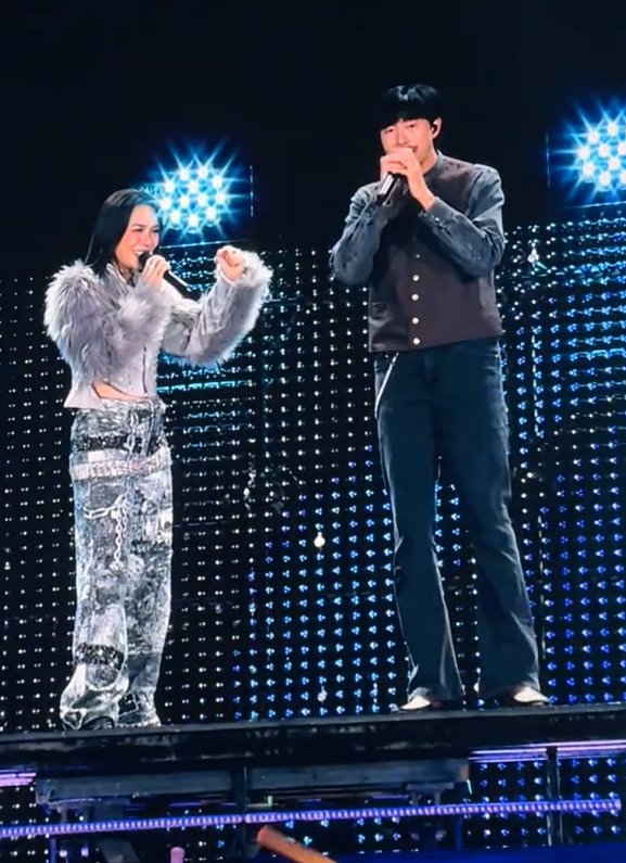 Giữa không khí sôi động của concert, rapper Đen Vâu vẫn giữ phong cách tối giản, quen thuộc làm nên thương hiệu của mình. Trên sân khấu, anh xuất hiện với bộ trang phục thoải mái, tập trung hoàn toàn vào âm nhạc. Đen Vâu phối một chiếc áo sơ mi denim tối màu khoác ngoài cùng áo gile nâu và quần jeans tối màu. Ảnh chụp màn hình 