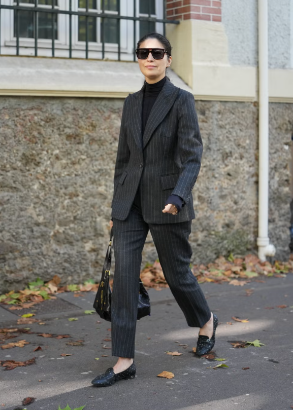 Thay áo sơ mi cài cúc bằng áo len cổ lọ mỏng để biến bộ vest kẻ sọc pinstripe trở nên hiện đại hơn. Kiểu phối này vừa giữ ấm cổ trước những cơn gió lạnh, vừa tạo điểm nhấn mùa đông cho set đồ công sở. Hoàn thiện trang phục với giày loafers da tối giản và túi dáng nửa vầng trăng, mang đến vẻ sành điệu cho phong cách phố thị. Ảnh: Harpers Bazaar