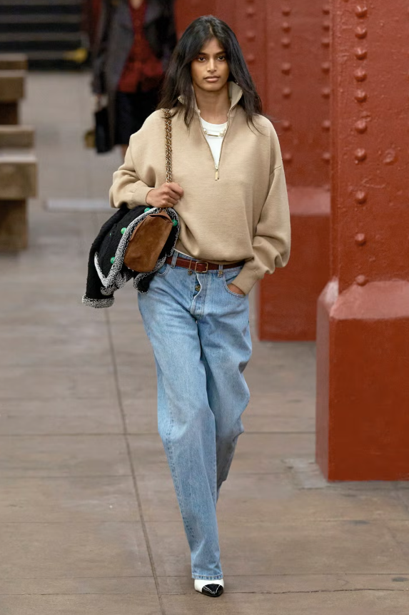 Quần jeans kết hợp áo len là công thức mặc đồ quen thuộc trong những tháng lạnh. Nhưng có một mẹo đơn giản giúp set đồ từ cơ bản trở nên tinh tế mà vẫn nhẹ nhàng: layering một chiếc áo thun cổ cao bên trong áo len khóa một phần. Việc để lớp áo cơ bản lộ ra dưới áo len tạo điểm nhấn thị giác rõ ràng, vừa có chủ ý lại vẫn giữ được vẻ trẻ trung, phóng khoáng. Ảnh: Elle