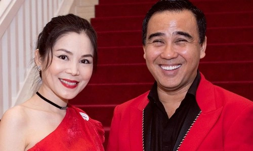 Vợ chồng Quyền Linh thường xuất hiện với phong cách lịch lãm, tinh tế. Một trong những lần nổi bật là hình ảnh trên thảm đỏ, khi nam MC diện vest đỏ rực rỡ phối cùng áo sơ mi đen bên trong, đường viền chỉ bạc tinh xảo tạo điểm nhấn sang trọng. Bộ vest này với phom dáng ôm vừa vặn, cổ vest sắc nét, mang đến vẻ ngoài mạnh mẽ, nam tính nhưng vẫn giữ được sự thanh lịch cần thiết. Đồng hành bên cạnh, nữ doanh nhân Dạ Thảo lựa chọn chiếc váy đỏ một vai với chất liệu satin mịn màng, phom dáng tôn đường cong tự nhiên. Màu đỏ chủ đạo không chỉ tạo sự đồng điệu rõ nét mà còn thể hiện sự hòa quyện hoàn hảo giữa hai cá tính: mạnh mẽ từ phía Quyền Linh và nữ tính, quyến rũ từ phía vợ. Sự kết hợp này mang lại tổng thể vừa nổi bật trên thảm đỏ, vừa không lấn át lẫn nhau.