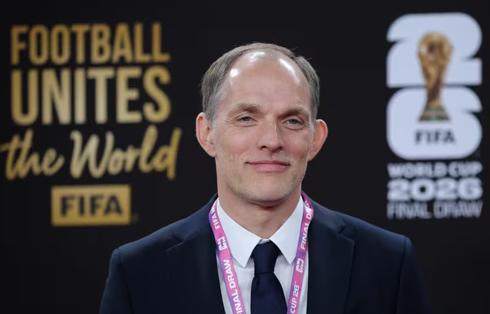 Thomas Tuchel nổi bật trên thảm đỏ World Cup 2026 với suit navy đậm, áo sơ mi trắng và cà vạt navy tối màu, kết hợp dây đeo badge sự kiện. Bộ suit có độ hoàn thiện cao với đường may tinh xảo, cổ bẻ ve nhọn sắc nét và túi áo xẻ tinh tế. Chi tiết này gợi nhớ đến các bộ suit từ Brioni hoặc Canali - những thương hiệu yêu thích của giới doanh nhân và HLV châu Âu. Ảnh: FIFA