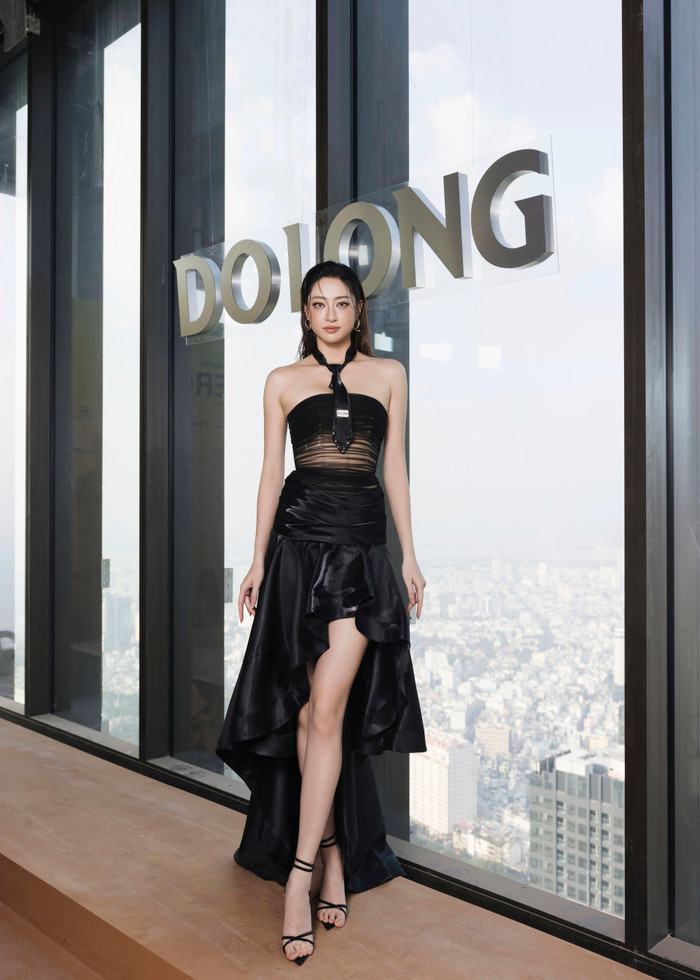 Hoa hậu Lương Thùy Linh diện một bộ đầm đen với phần thân trên là áo quây kết hợp chi tiết xuyên thấu và cà vạt mảnh. Phần chân váy có kiểu dáng high-low với chất liệu satin tạo độ bồng bềnh, hoàn thiện vẻ ngoài thanh lịch nhưng đầy cá tính và hiện đại. Ảnh: FBNV