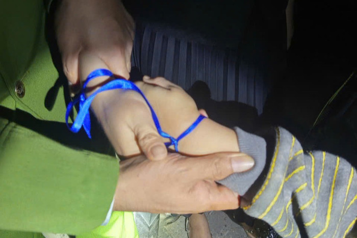 Tay của người phụ nữ và cháu bé có buộc bằng dây màu xanh. Ảnh: Bộ Công an