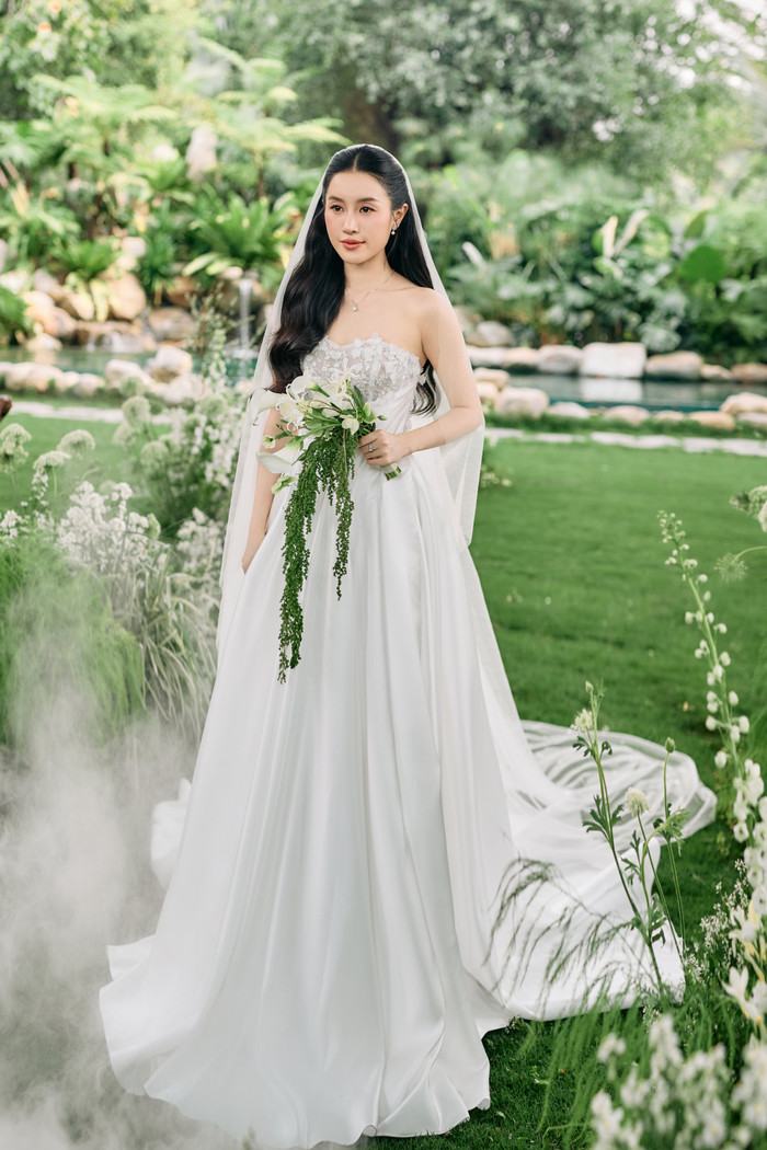 Bước vào lễ đường, bạn đời của Vũ Cát Tường xuất hiện lộng lẫy trong chiếc váy cưới trắng tinh khôi với thiết kế cúp ngực tôn lên bờ vai thanh mảnh và nét đẹp duyên dáng. Phần thân trên của váy được nhấn nhá bằng họa tiết ren tinh tế, hòa quyện cùng chất liệu lụa mềm mại làm tổng thể trở nên thanh thoát và sang trọng.