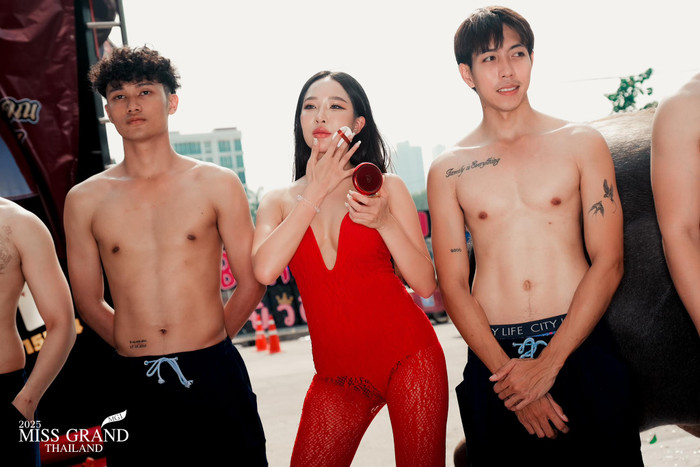 Một người đẹp khác xuất hiện tại họp báo khởi động Miss Grand Thailand 2025 với bộ jumpsuit bó sát, mang tông màu đỏ rực và có chi tiết khoét sâu, để lộ lấp ló 'gò bồng đảo'. Thiết kế này bị đánh giá phản cảm, không phù hợp khi xuất hiện tại sự kiện. Không những vậy, cô còn đưa dàn người mẫu nam ngực trần đến cùng. (Ảnh: Miss Grand Thailand)