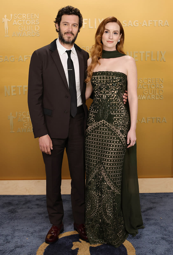 Adam Brody (trái) và Leighton Meester xuất hiện trong những thiết kế đẳng cấp. Leighton Meester chọn một chiếc váy Elie Saab màu xanh rêu với họa tiết ren tinh xảo, phần cổ quấn nhẹ nhàng tạo điểm nhấn thanh lịch, giúp cô toát lên vẻ đẹp quyến rũ và cổ điển. Đi bên cạnh, Adam Brody lịch lãm trong bộ suit màu nâu trầm từ Prada, kết hợp cà vạt đen và giày da bóng, tạo nên hình ảnh nam tính và sang trọng.