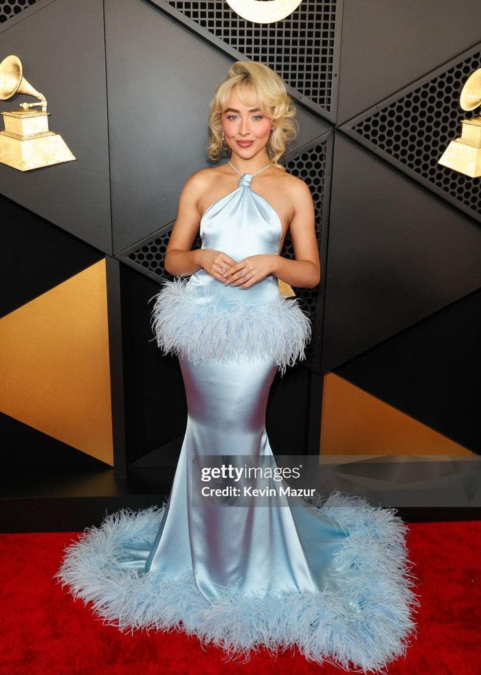 Sabrina Carpenter xuất hiện lộng lẫy tựa minh tinh cổ điển. Nữ ca sĩ khoác lên người chiếc váy cổ yếm, ôm sát vóc dáng chuẩn chỉnh. Thiết kế này tăng thêm phần sang trọng với chi tiết lông vũ đính kết quanh hông và phần đuôi váy. 