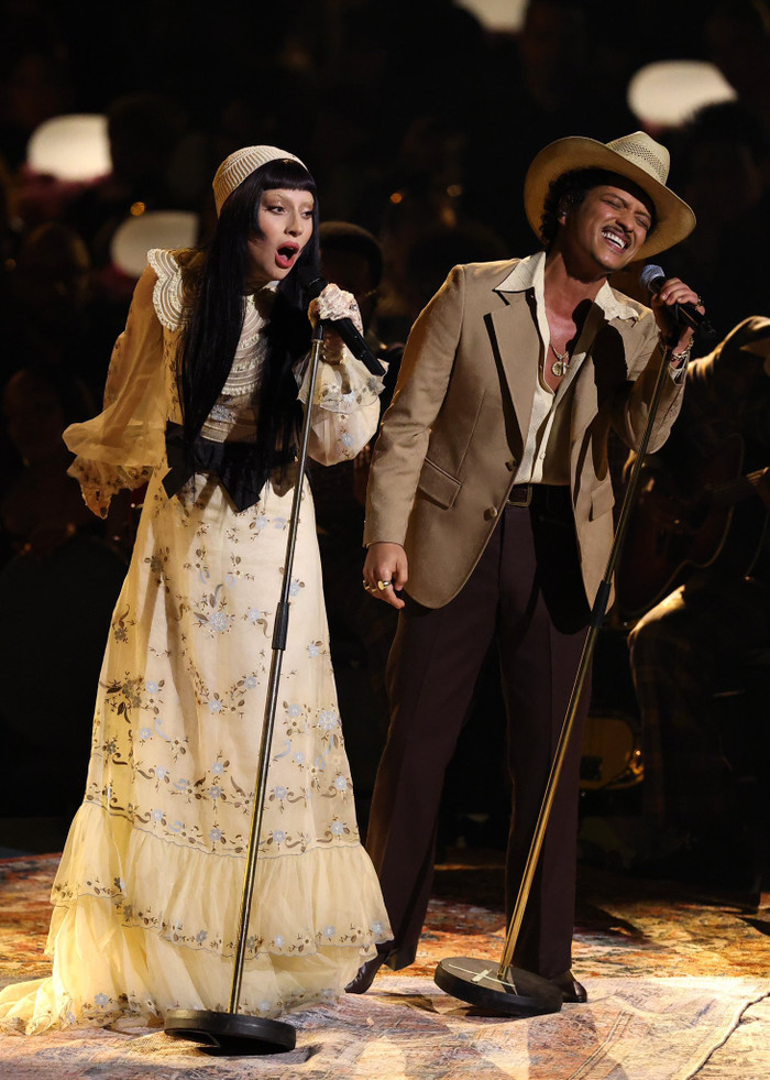 Lady Gaga cùng Bruno Mars thể hiện tiết mục song ca. Khác hẳn với hình tượng quái dị hay hở bạo trước đó, Lady Gaga bất ngờ theo đuổi phong cách ngọt ngào đến lạ thường. Nữ ca sĩ diện mẫu váy dài, che kín vóc dáng. Trang phục này được điểm xuyến họa tiết hoa nhí, mang cảm hứng cổ điển. Về phần Bruno Mars, nam ca sĩ diện bản phối thời trang thanh lịch gồm quần tây, áo sơ mi và áo khoác blazer thuộc tông màu nâu chủ đạo. (Ảnh: Getty Images)