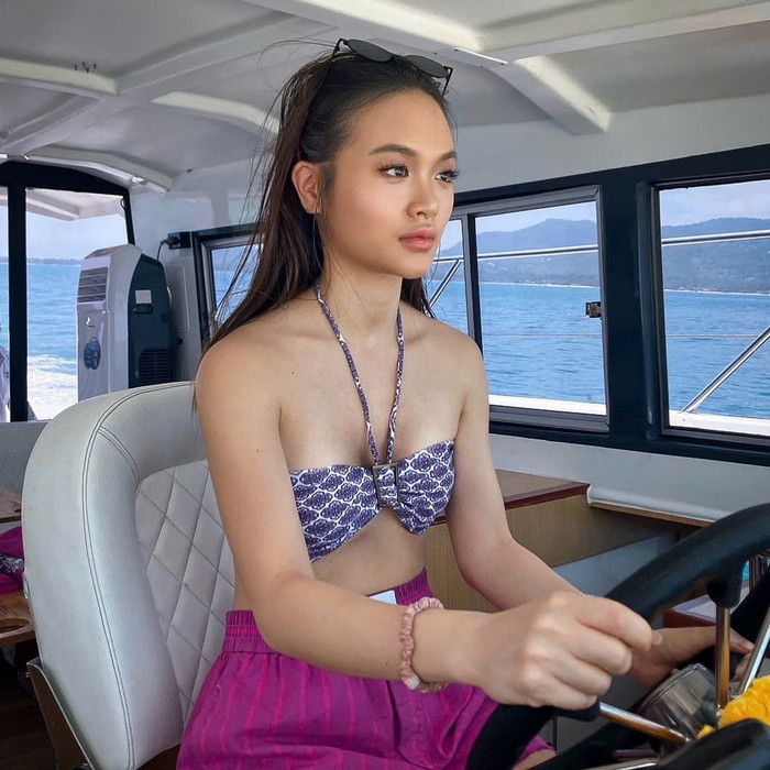 Xuất hiện trên du thuyền, con gái Madam Pang chọn phong cách thời trang biển tối giản nhưng đầy ấn tượng. Áo bikini dạng quây với họa tiết địa phương độc đáo, nhấn nhá bằng nơ trung tâm, giúp tôn lên vẻ nữ tính và gợi cảm. Nuanwan Phanchet kết hợp cùng quần ngắn màu hồng fuchsia tạo nên tổng thể trang phục vừa mang hơi thở trẻ trung, vừa thể hiện sự sang trọng tinh tế. Kính râm và vòng tay tạo điểm nhấn nhẹ nhàng, hoàn thiện phong cách thời trang đẳng cấp. 