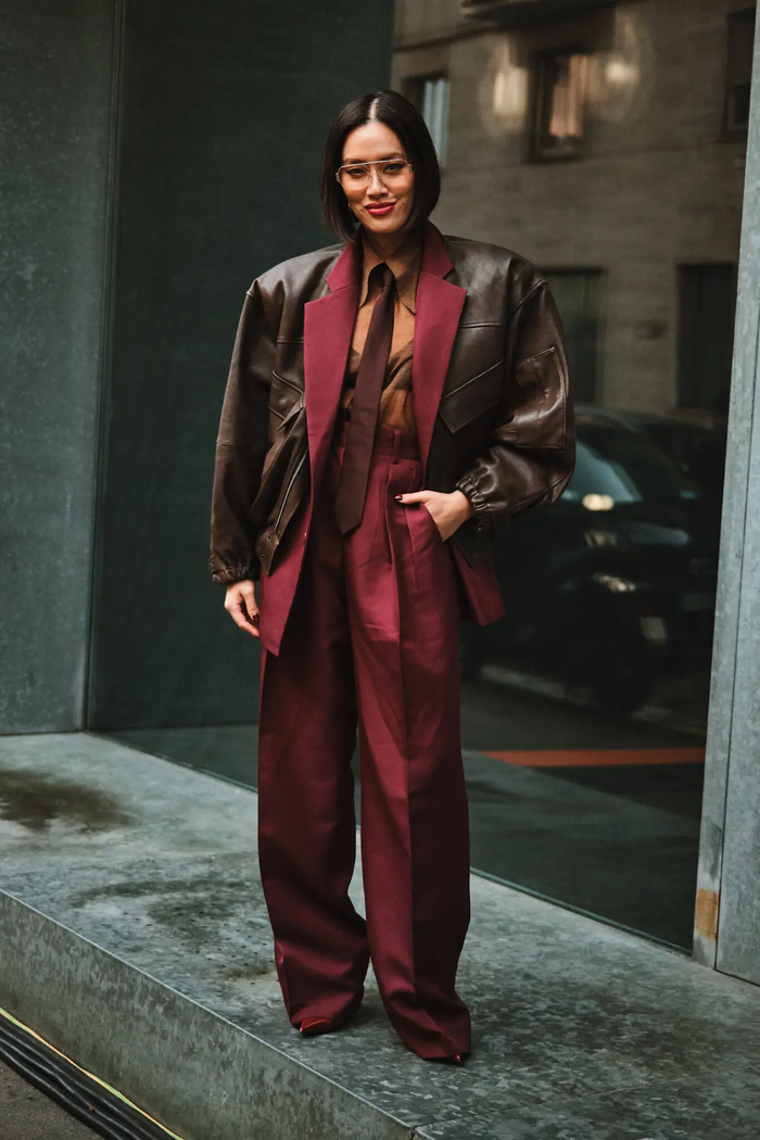 Cô gái trẻ trong phong cách “Girlboss” kết hợp giữa bộ suit đỏ burgundy cùng chiếc áo khoác bomber da đứng form màu nâu đất. Bên trong là chiếc sơ mi xuyên thấu màu nâu bò kèm cà vạt màu đỏ nâu. Tổng thể gợi lên sự cá tính nhưng vẫn thanh lịch và trưởng thành. Đây cũng là một cách phối màu cực kỳ bắt mắt của màu đỏ burgundy đang rất nổi dạo gần đây