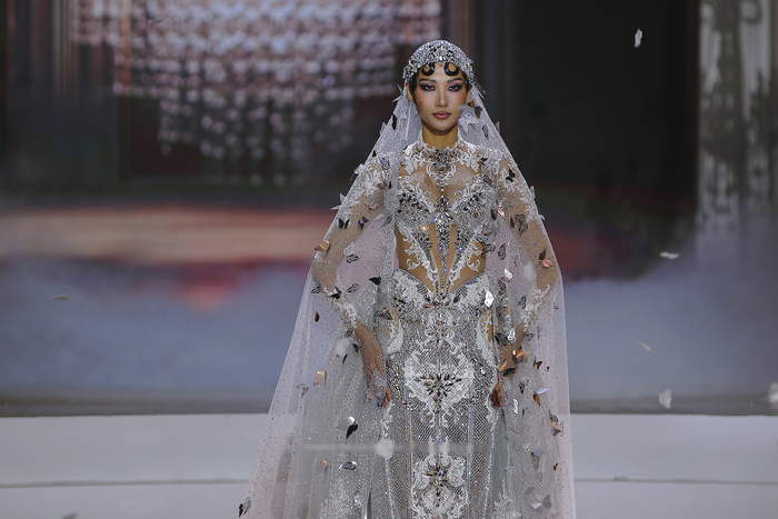 Thân váy dạ hội ôm sát được bao phủ hoàn toàn bởi hàng ngàn viên đá, pha lê và cườm bạc, tạo nên những hoa văn đối xứng phức tạp trên nền vải xuyên thấu, với những khoảng hở (cut-out) tinh tế ở eo và vai, tăng thêm vẻ quyến rũ. 