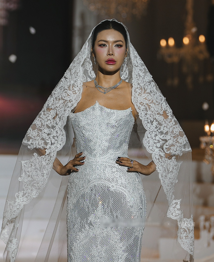 Xuyên suốt 45 looks, nhà thiết kế cho thấy sự nắm bắt xu hướng, đưa chất liệu ren trở lại đường đua 'bridal' bằng cách điểm xuyết trên cả trang phục lẫn veil tóc. Thiết kế váy cúp ngực ôm sát cơ thể mà Minh Tú khoác trên người được bao phủ bởi vô số viên đá, pha lê lấp lánh, nhưng đặc biệt, các họa tiết ren tinh xảo, đồng điệu với khăn voan, được khéo léo lồng ghép trên bề mặt váy, từ phần cúp ngực xuống thân váy. Sự kết hợp này không chỉ tôn vinh đường cong quyến rũ của Minh Tú mà toát lên thần thái mạnh mẽ, hiện đại đặc trưng của cô. 