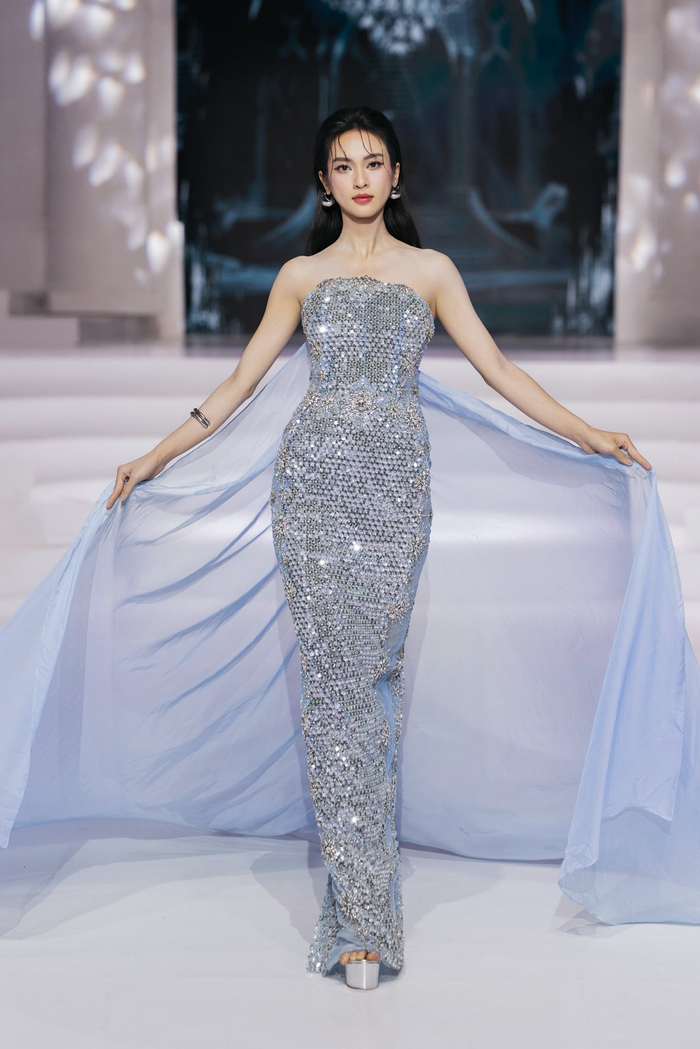 Á hậu Vũ Thúy Quỳnh diện thiết kế dạ hội ánh bạc phối xanh băng, ôm dáng và đính đá đều tay, kết hợp phần voan tay buông nhẹ tạo cảm giác dịu dàng, thanh lịch. Tuy nhiên, tổng thể chưa đủ tạo điểm nhấn rõ rệt – từ phom dáng đến màu sắc đều khá an toàn, thiếu sự bứt phá cần có cho một sân khấu thời trang đòi hỏi cá tính. Đây là kiểu đầm dễ mặc nhưng dễ hòa lẫn.