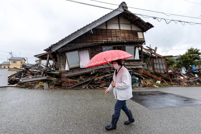 Một người phụ nữ cầm ô đi dưới trời mưa ngang qua một ngôi nhà bị hư hại nặng nề do trận động đất ở Bán đảo Noto gây ra vào ngày 31 tháng 12 năm 2024 tại Suzu, Nhật Bản. (Buddhika Weerasinghe/Getty Images).