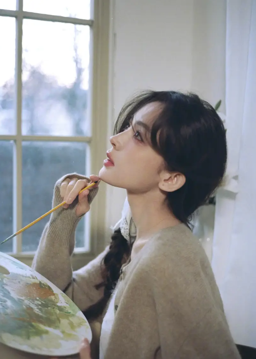 Cổ Lực Na Trát tạo dáng nhẹ nhàng bên giá vẽ, tay cầm cọ.