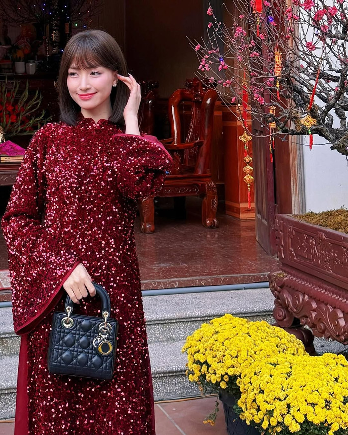 Mẫu thứ ba mà Hòa Minzy diện trong dịp Tết là áo dài màu đỏ sequin lấp lánh toàn thân. Chất liệu sequin phủ kín tạo hiệu ứng ánh sáng bắt mắt, tay áo loe rộng, phần thân áo dài được thiết kế dài chấm gót với đường cắt cổ điển. Màu đỏ kết hợp cùng hiệu ứng sequin giúp mẫu áo dài này trở nên nổi bật trong không gian tiệc gia đình hoặc chúc Tết. Thiết kế này khiến nhiều người nhận ra áo dài không nhất thiết phải đơn giản mới đẹp; khi được biến tấu bằng chất liệu lấp lánh, nó vẫn giữ được sự trang nhã mà vẫn tạo điểm nhấn mạnh mẽ. Ảnh: IGNV
