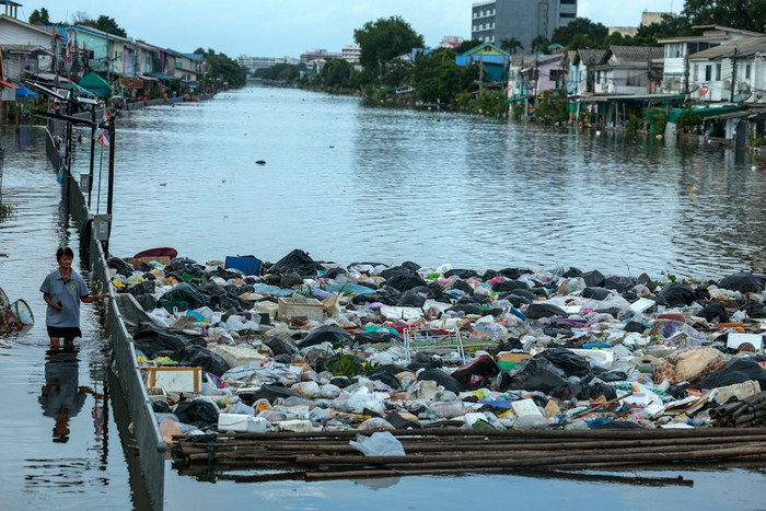 Ngày 28 tháng 9 năm 2026, tại Bangkok, Thái Lan, một người phụ nữ lội qua vùng nước lũ gần một đống rác sau trận mưa lớn. (Reuters).