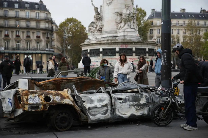 Người dân đứng xem một chiếc xe bị cháy rụi ở trung tâm Paris sau một đêm yên tĩnh hôm thứ Hai trong thời gian giới nghiêm (Christophe Ena).