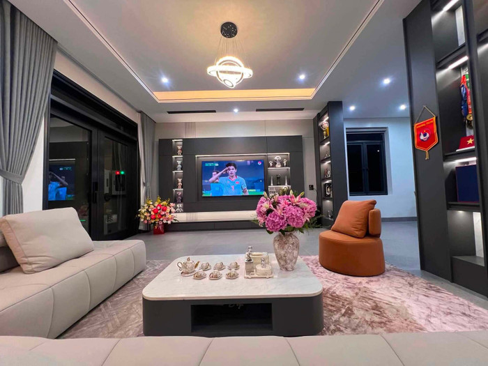 Phòng khách gây chú ý với hệ kệ tivi thiết kế âm tường. Các ô trưng bày được bố trí chạy gần sát trần, sử dụng gam xám đậm tạo điểm nhấn cho tổng thể không gian. Phần kệ được thiết kế liền khối, vừa tăng khả năng lưu trữ vừa giúp phòng khách có cảm giác gọn gàng. Hiện căn phòng đã cơ bản hoàn thiện phần trần, tường và hệ tủ, chờ bổ sung thêm các món nội thất.