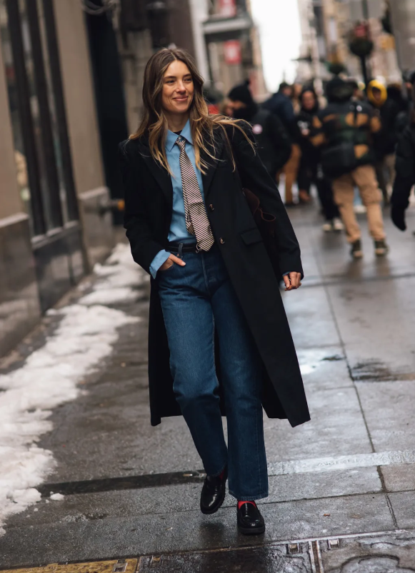 Aemilia Madden cho thấy đôi khi sự tối giản lại tạo hiệu quả rõ rệt trong phong cách. Cô kết hợp áo khoác đen, jeans ống đứng và cà vạt trên nền áo xanh, hoàn thiện bằng giày lười và tất. Launchmetrics