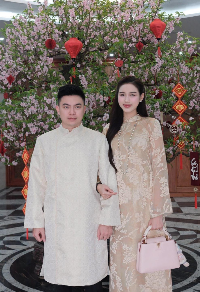 Cặp đôi Hoa hậu Đỗ Thị Hà và thiếu gia Viết Vương lựa chọn tông be - kem nhã nhặn làm chủ đạo. Ông xã Đỗ Hà diện áo dài gấm màu kem họa tiết chìm lịch lãm, trong khi nàng hậu lại nổi bật với áo dài nude in hoa lớn, phối vòng cổ ngọc trai và túi hồng pastel đầy sang trọng. Ảnh: FBNV