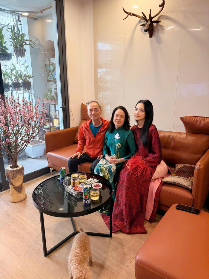 Hoa hậu Hương Giang diện áo dài đỏ đô họa tiết chìm, tay đính lông nhẹ tạo điểm nhấn mềm mại và nổi bật bên bố mẹ. Ảnh: FBNV