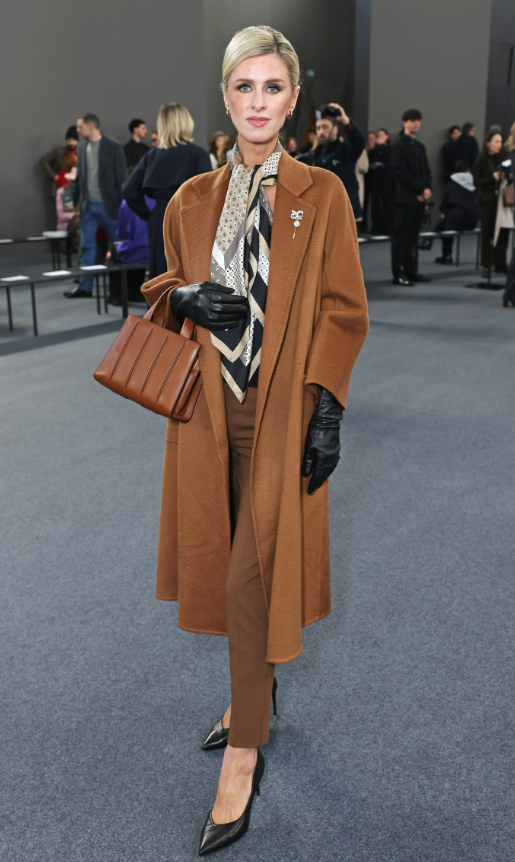 Nicky Hilton Rothschild diện bộ suit tông nâu được phối layering tinh tế với sơ mi và khăn lụa họa tiết buộc cổ. Găng tay da đen và túi xách đồng điệu mang đến phong thái quý phái, cổ điển. Ảnh: Getty Images
