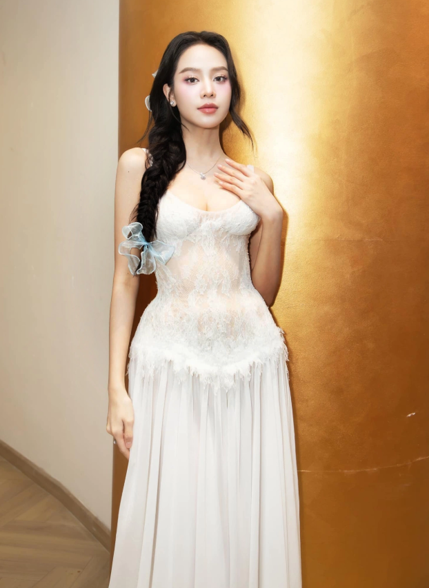 Hoa hậu Thanh Thủy hóa thân thành hình ảnh “nàng thơ” khi diện thiết kế đầm ren trắng với phần thân trên xuyên thấu nhẹ, đính họa tiết tinh xảo, kết hợp chân váy voan xếp ly mềm mại tạo cảm giác bay bổng. Phom hai dây cúp ngực giúp cô khéo khoe bờ vai thon, đặc biệt khi đi cùng kiểu tóc tết lệch và nơ xanh, mang đến vẻ đẹp trẻ trung, dịu dàng và đầy trong trẻo. Ảnh: FBNV