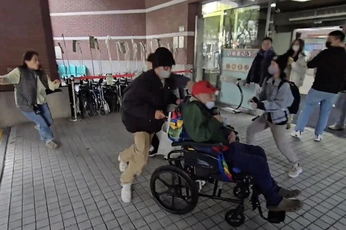 Cụ ông họ Vương (ngồi xe lăn và đội mũ đỏ) đã kết hôn với người chăm sóc mình, bà Lai (người đầu tiên từ trái sang), vào tháng Giêng. Mới đây, các con của ông đã cố gắng 'giải cứu' ông bên ngoài bệnh viện trong lúc ông đang có lịch hẹn khám bệnh. (Ảnh do công chúng cung cấp)