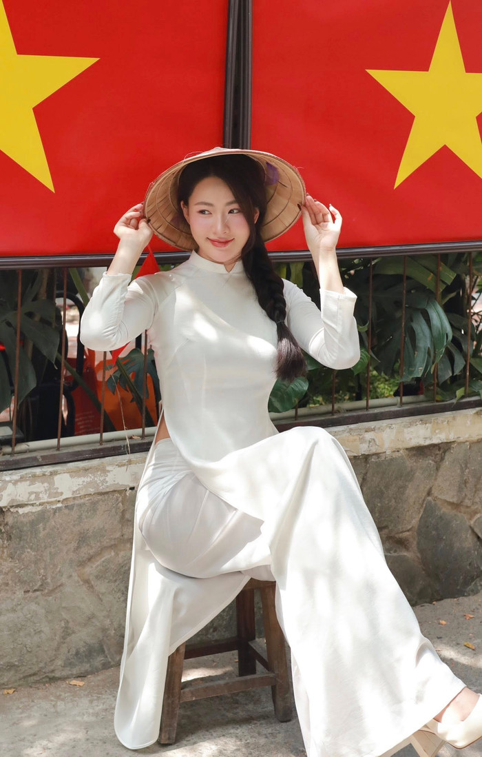 Thiết kế áo dài trắng cổ điển, ôm dáng vừa phải, được Minh Trang phối cùng nón lá, gợi hình ảnh người con gái Việt dịu dàng, nền nã. Kiểu tóc tết lệch và quần lụa trắng giúp tổng thể thêm phần duyên dáng, mang hơi thở hoài niệm rõ nét. Ảnh: FBNV