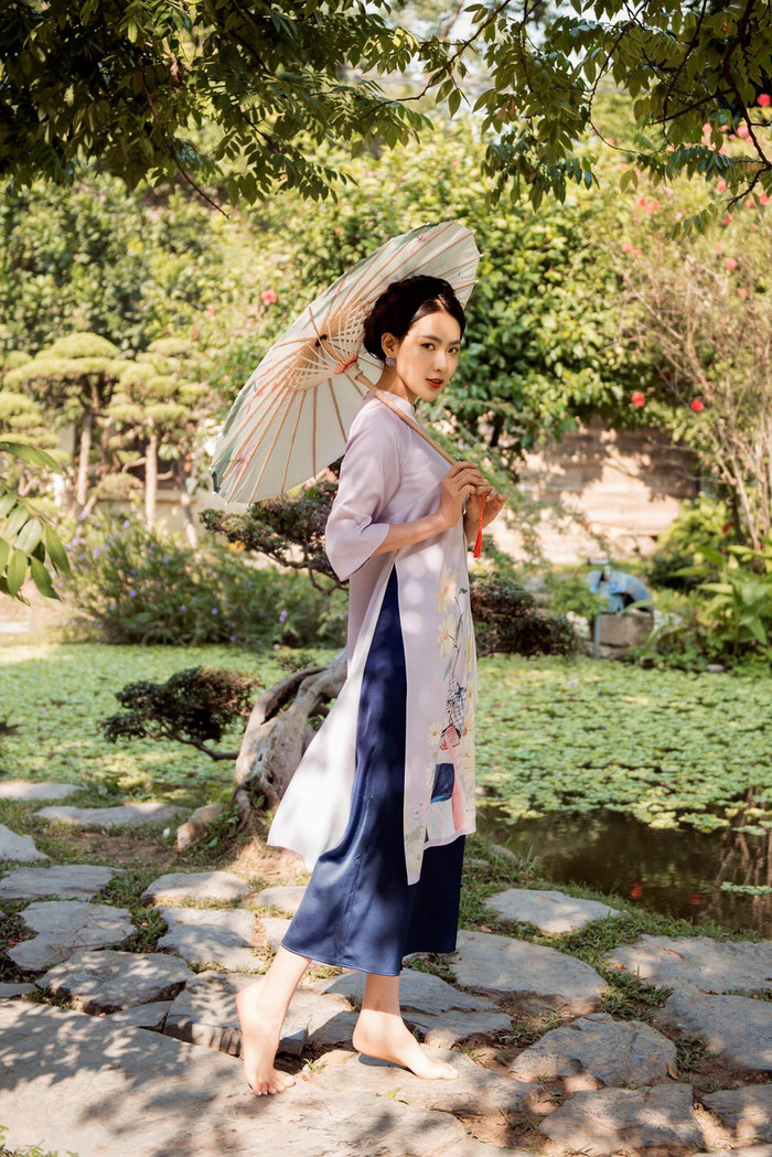 Khép lại là hình ảnh áo dài tím nhạt in họa tiết tranh vẽ nghệ thuật, phối cùng quần lụa xanh đậm tạo sự tương phản hài hòa. Chiếc ô giấy truyền thống càng làm nổi bật tinh thần Á Đông, tôn lên vẻ kín đáo, thanh thoát nhưng vẫn đầy cuốn hút của Minh Trang. Ảnh: FBNV