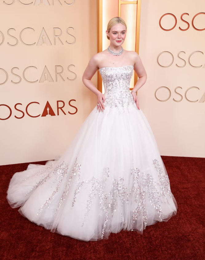 Elle Fanning tỏa sáng trong váy dạ hội trắng cúp ngực dáng công chúa, thân váy đính họa tiết ánh kim tinh xảo và chân váy tulle bồng bềnh. Cô hoàn thiện vẻ ngoài lãng mạn với trang sức đặt may riêng của Givenchy cùng các món trang sức cổ điển. Ảnh: Harpers Bazaar