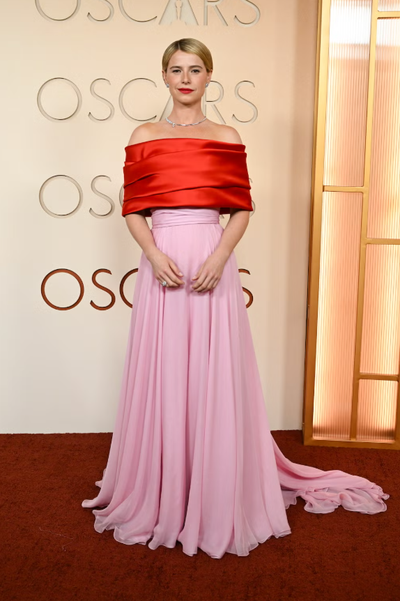 Jessie Buckley đầy nổi bật trong thiết kế đặt làm riêng của Chanel cùng trang sức đồng điệu. Bộ trang phục gây chú ý với áo choàng đỏ trễ vai ở phần thân trên, cùng chân váy dài màu hồng pastel mềm mại. Ảnh: Harpers Bazaar